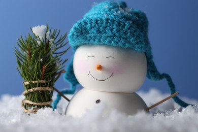 Photo of Cute decorative snowman and fir tree branches on artificial snow against light blue background, closeup