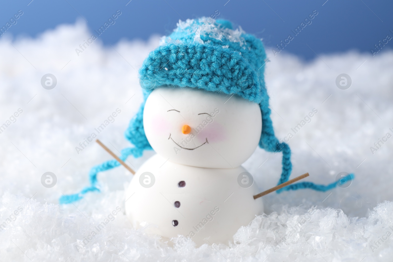 Photo of Cute decorative snowman on artificial snow against light blue background, closeup