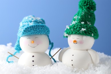 Photo of Cute decorative snowmen on artificial snow against light blue background, closeup