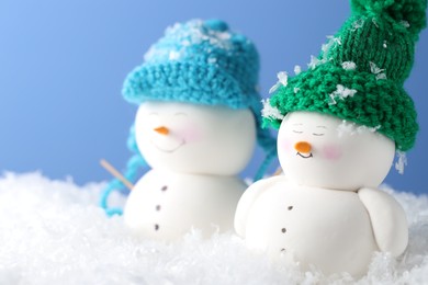 Photo of Cute decorative snowmen on artificial snow against light blue background, closeup