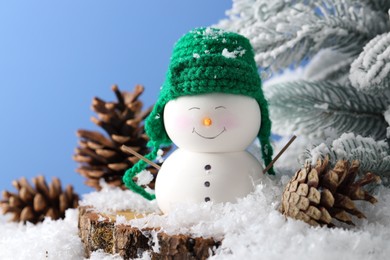 Photo of Cute decorative snowman, fir tree branches and cones on artificial snow against light blue background, closeup