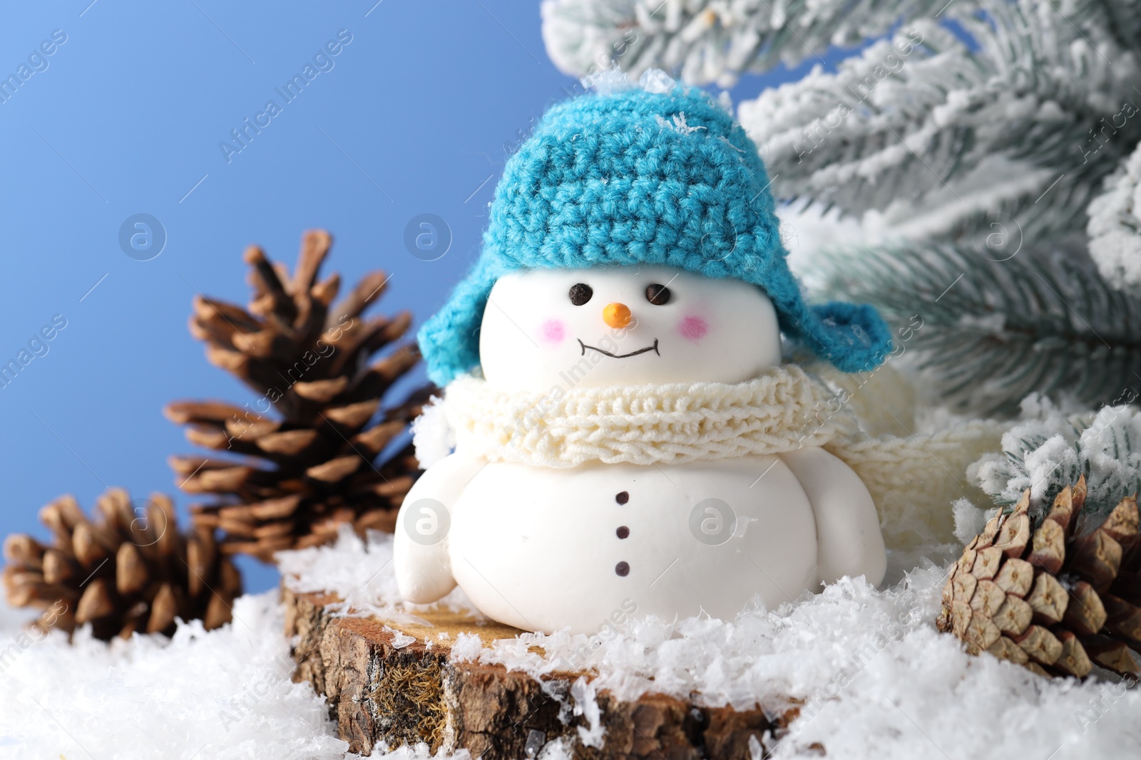 Photo of Cute decorative snowman, fir tree branches and cones on artificial snow against light blue background, closeup