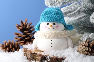 Photo of Cute decorative snowman, fir tree branches and cones on artificial snow against light blue background, closeup