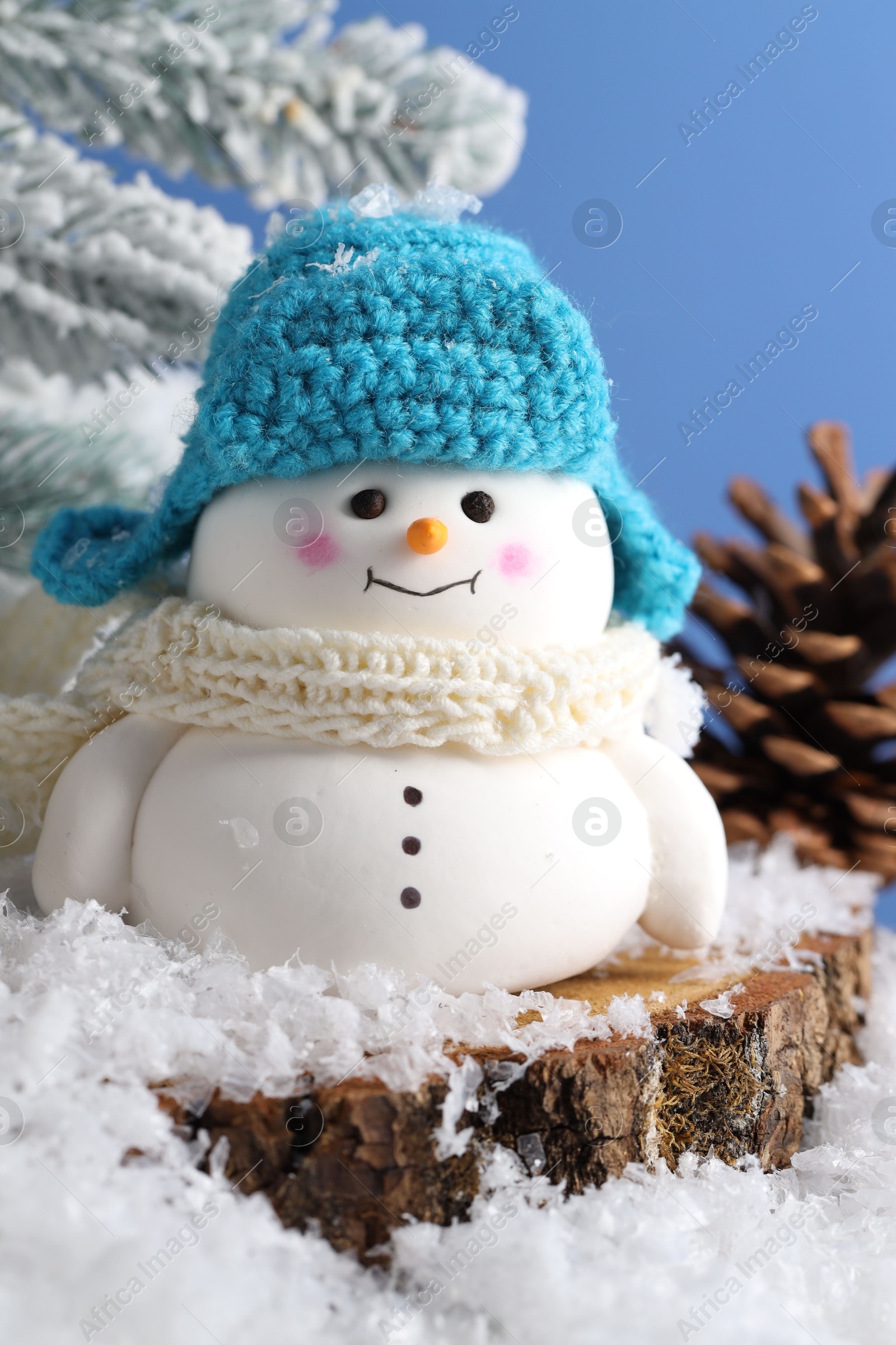 Photo of Cute decorative snowman, fir tree branches and cone on artificial snow against light blue background, closeup