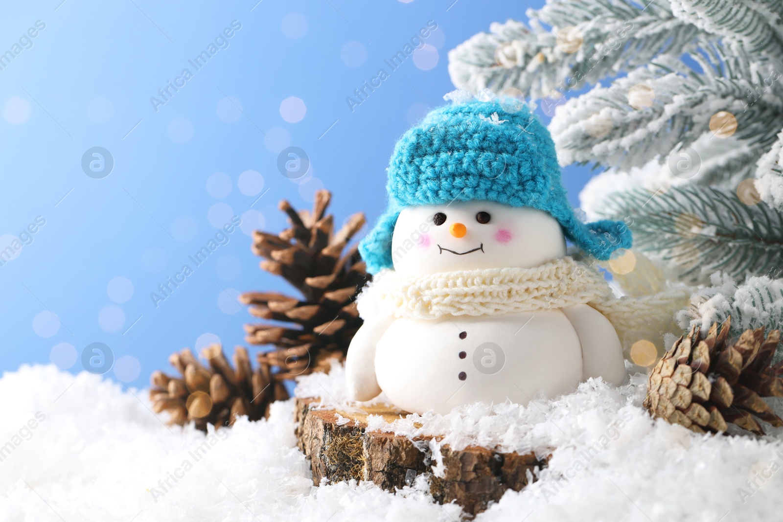 Photo of Cute decorative snowman, fir tree branches and cones on artificial snow against light blue background, closeup. Space for text