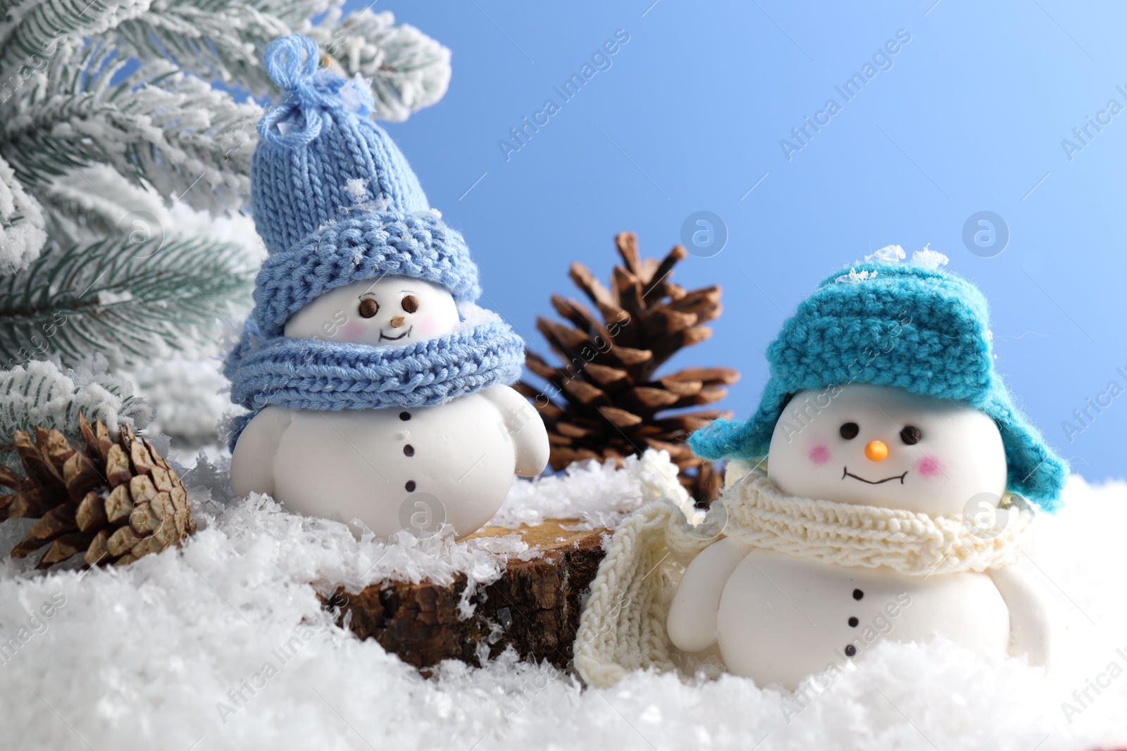 Photo of Cute decorative snowmen, fir tree branches and cones on artificial snow against light blue background, closeup