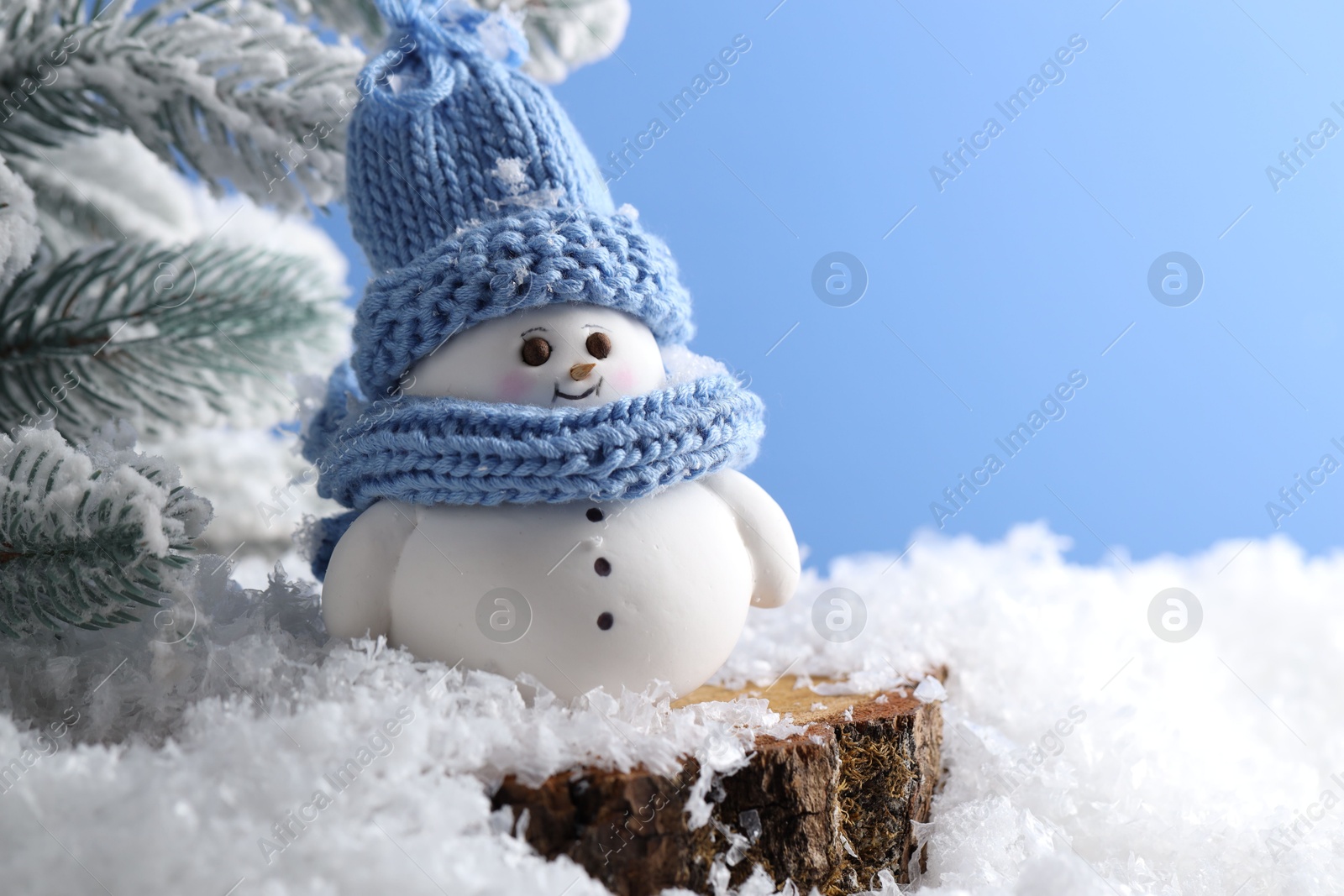 Photo of Cute decorative snowman and fir tree branches on artificial snow against light blue background, closeup. Space for text