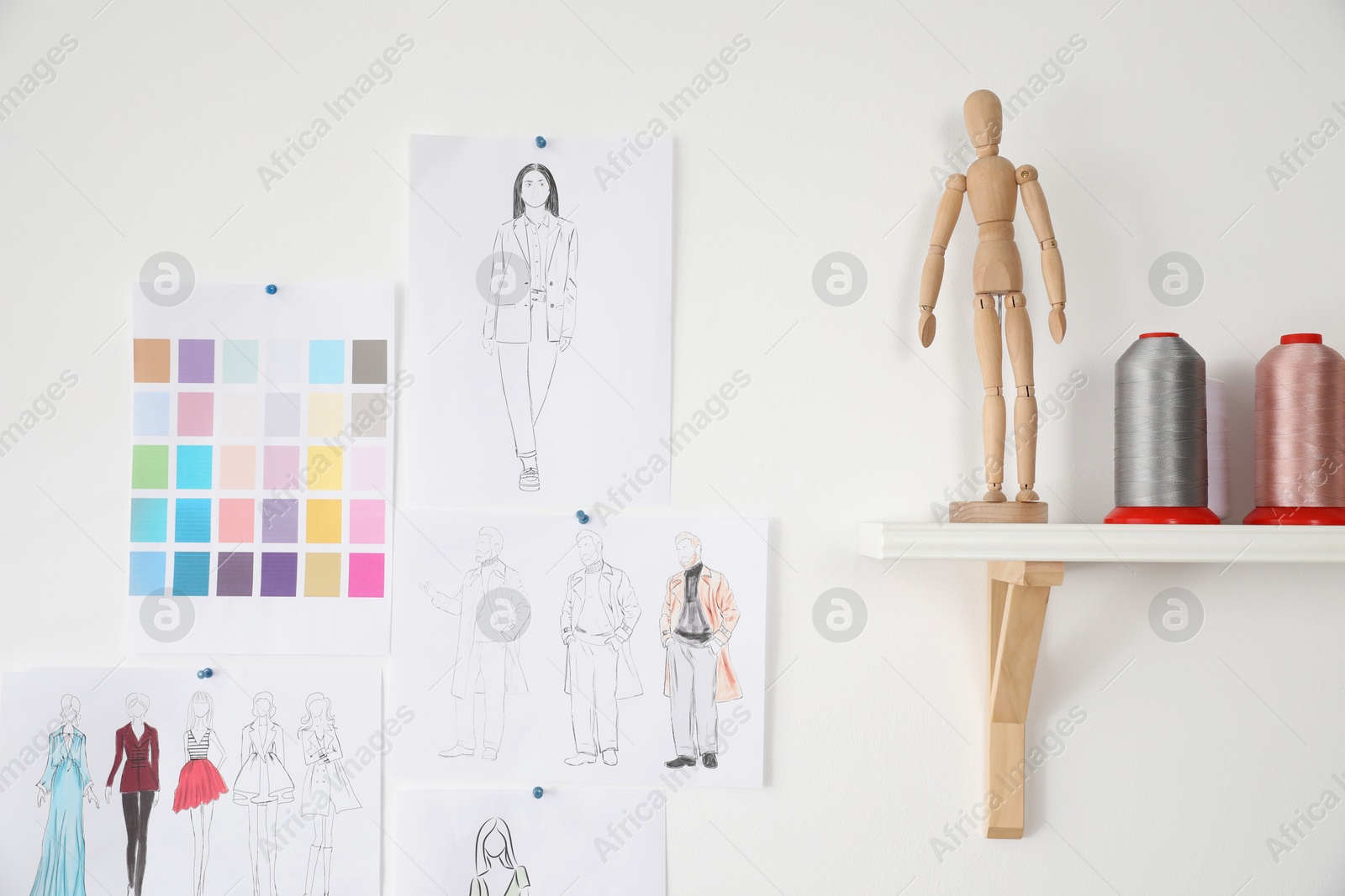 Photo of Different sketches of new outfits on white wall and threads in fashion designer`s workshop