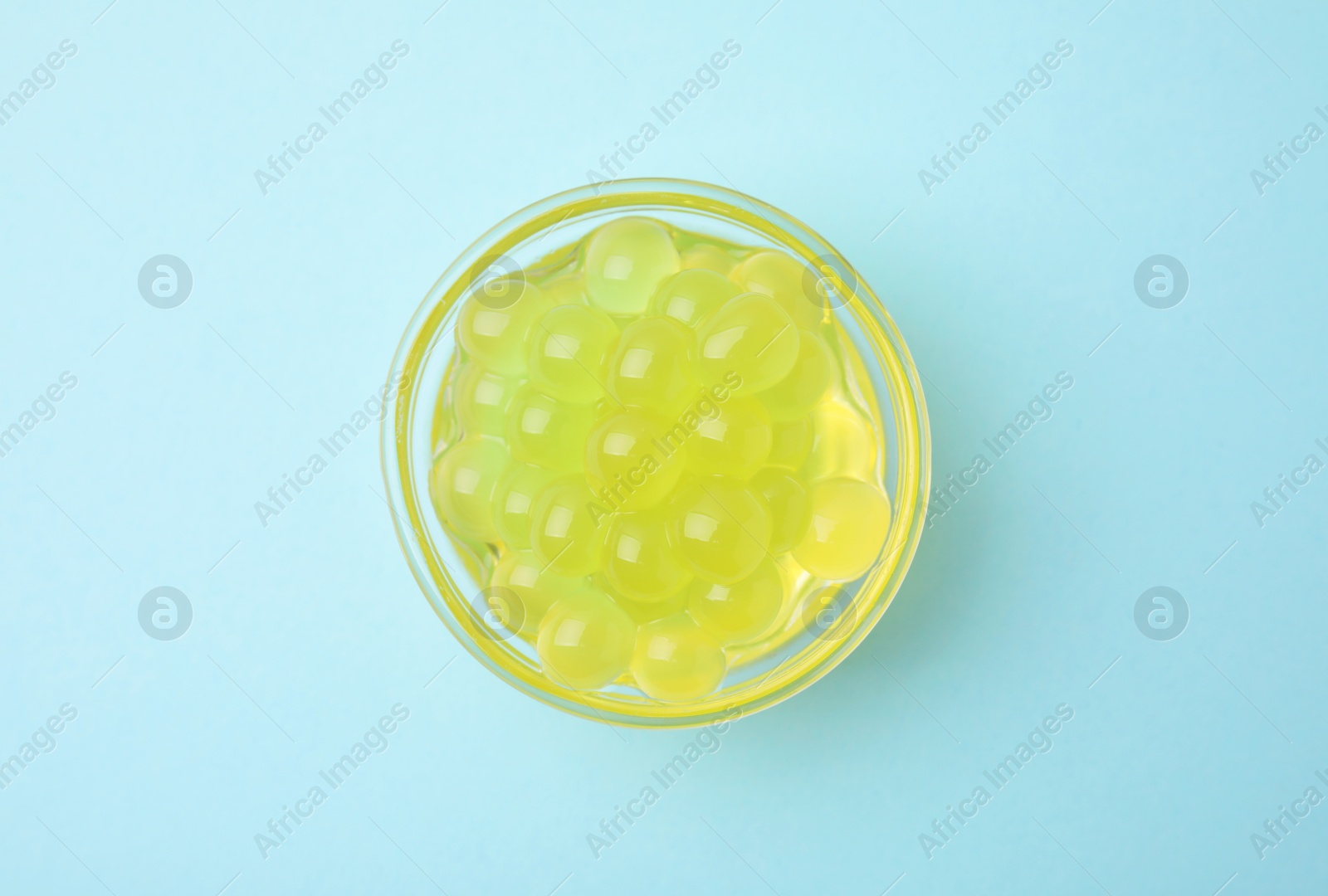 Photo of Bright tapioca pearls in bowl on light blue background, top view