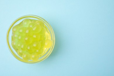 Photo of Bright tapioca pearls in bowl on light blue background, top view. Space for text