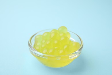 Photo of Bright tapioca pearls in bowl on light blue background, closeup