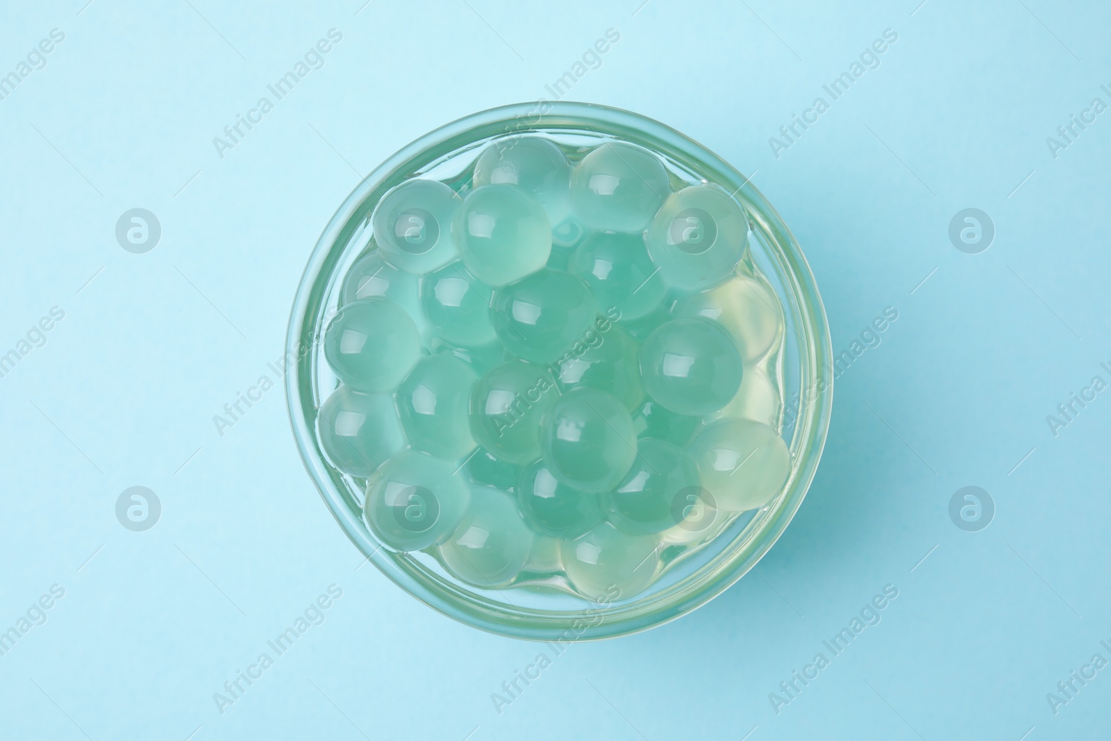 Photo of Bright tapioca pearls in bowl on light blue background, top view