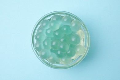 Photo of Bright tapioca pearls in bowl on light blue background, top view