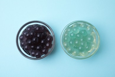 Photo of Color tapioca pearls in bowls on light blue background, flat lay