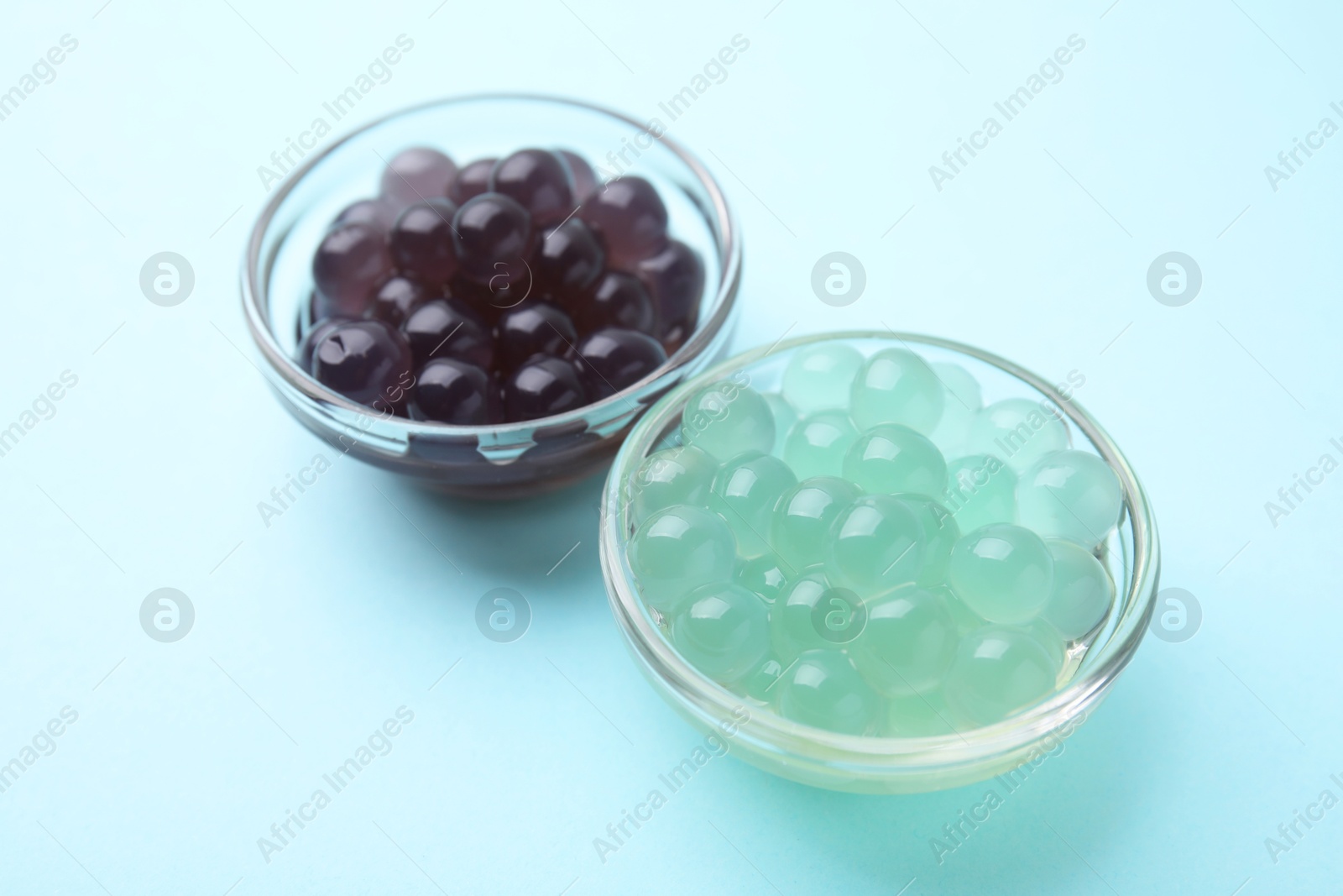 Photo of Color tapioca pearls in bowls on light blue background, closeup