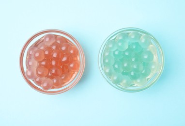 Photo of Bright tapioca pearls in bowls on light blue background, flat lay