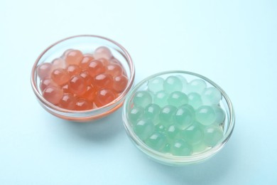 Photo of Bright tapioca pearls in bowls on light blue background, closeup