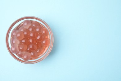 Photo of Bright tapioca pearls in bowl on light blue background, top view. Space for text