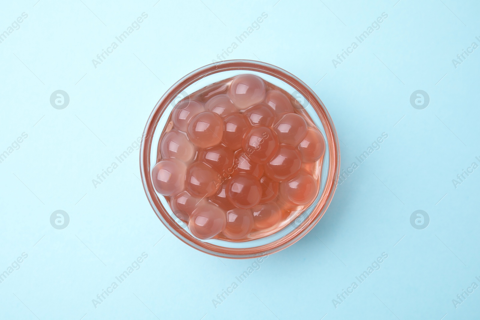 Photo of Bright tapioca pearls in bowl on light blue background, top view