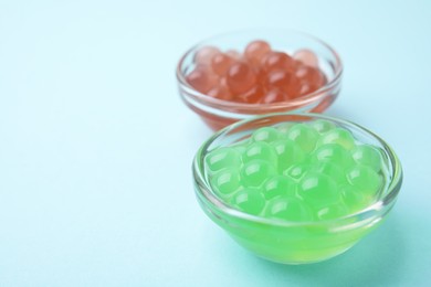 Photo of Bright tapioca pearls in bowls on light blue background, closeup. Space for text