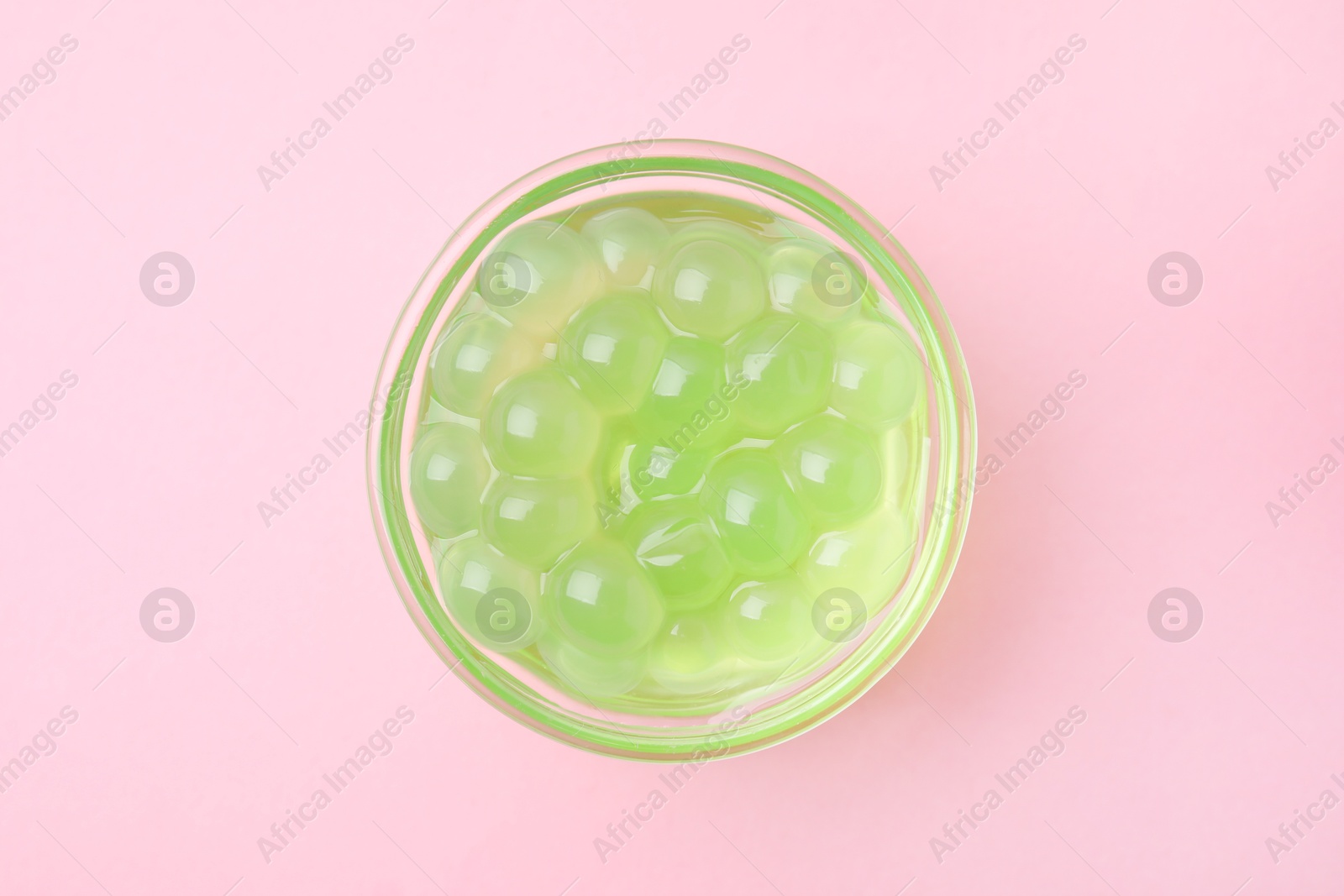 Photo of Bright tapioca pearls in bowl on pink background, top view