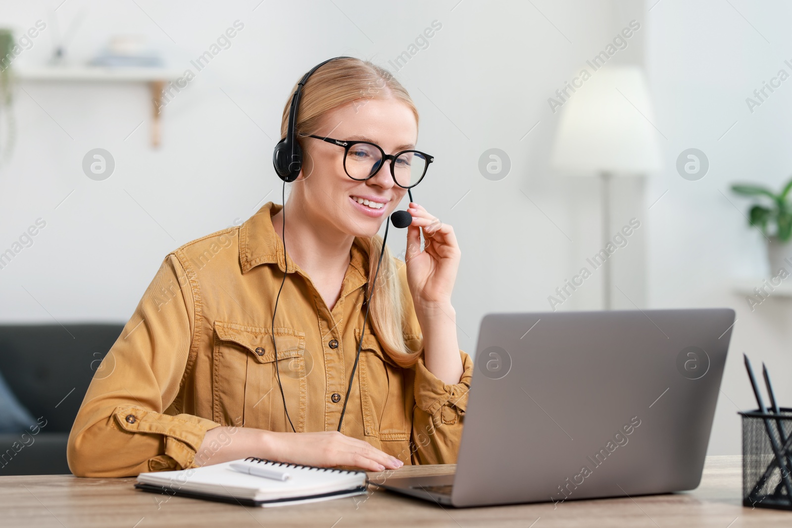 Photo of Interpreter in headset having video chat via laptop at table indoors