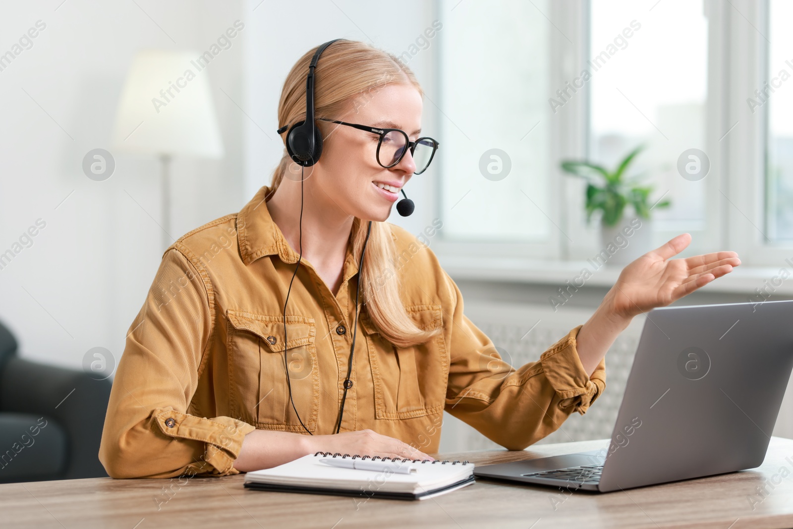 Photo of Interpreter in headset having video chat via laptop at table indoors