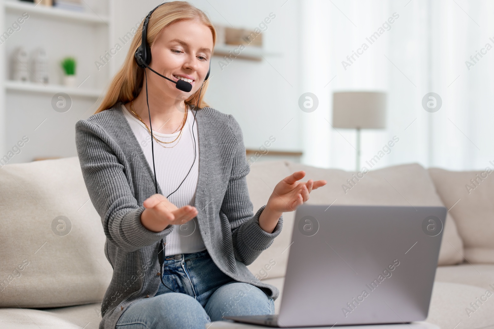 Photo of Interpreter in headset having video chat via laptop on sofa at home