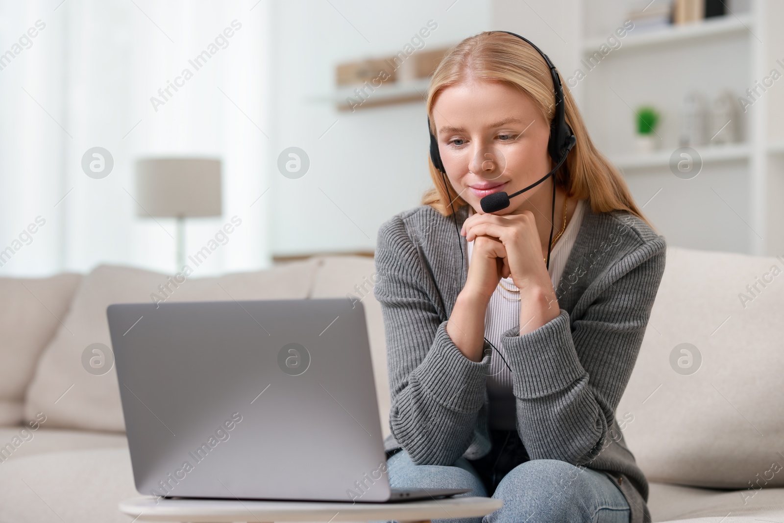 Photo of Interpreter in headset having video chat via laptop on sofa at home