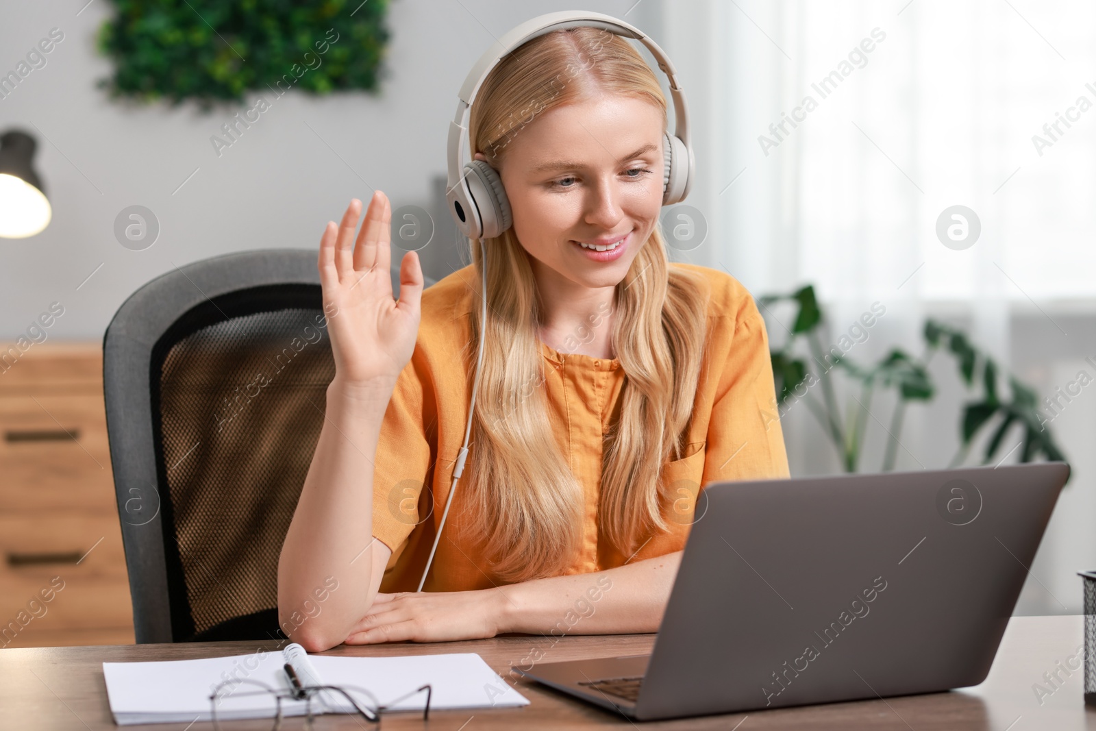 Photo of Interpreter in headphones having video chat via laptop at table indoors