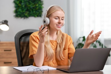 Interpreter in headphones having video chat via laptop at table indoors