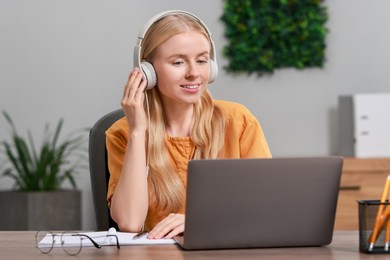 Photo of Interpreter in headphones working with laptop at table indoors