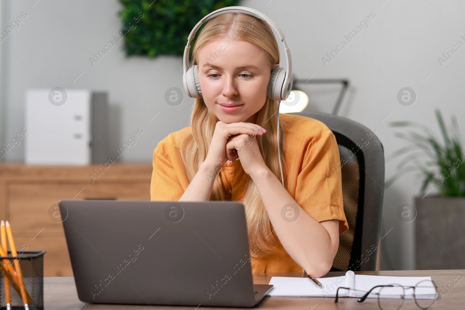 Photo of Interpreter in headphones working with laptop at table indoors