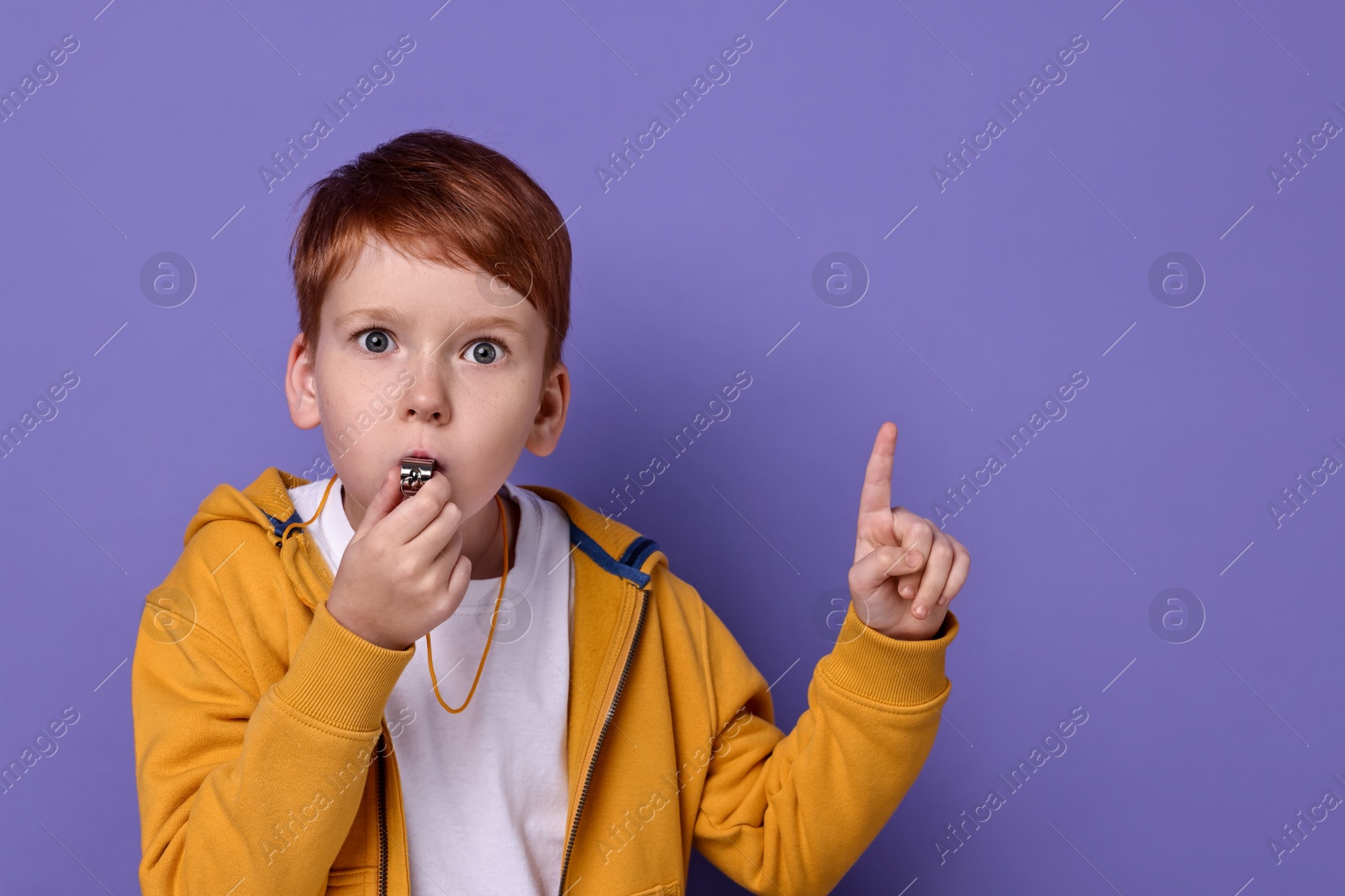 Photo of Little boy blowing whistle on purple background