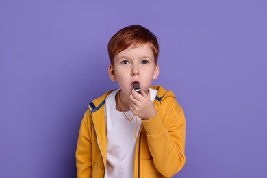 Photo of Little boy blowing whistle on purple background