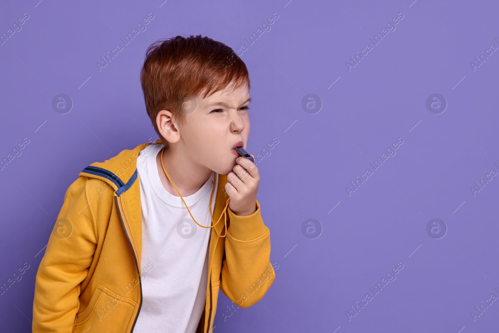 Photo of Little boy blowing whistle on purple background, space for text