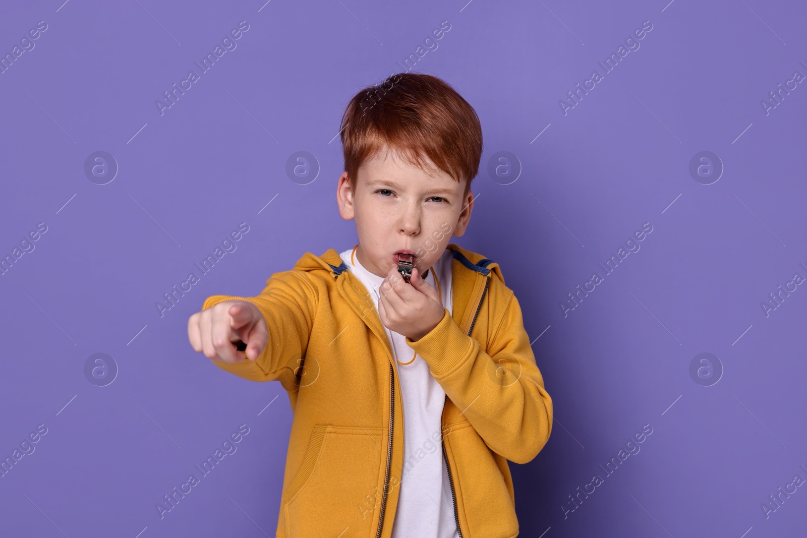 Photo of Little boy blowing whistle on purple background