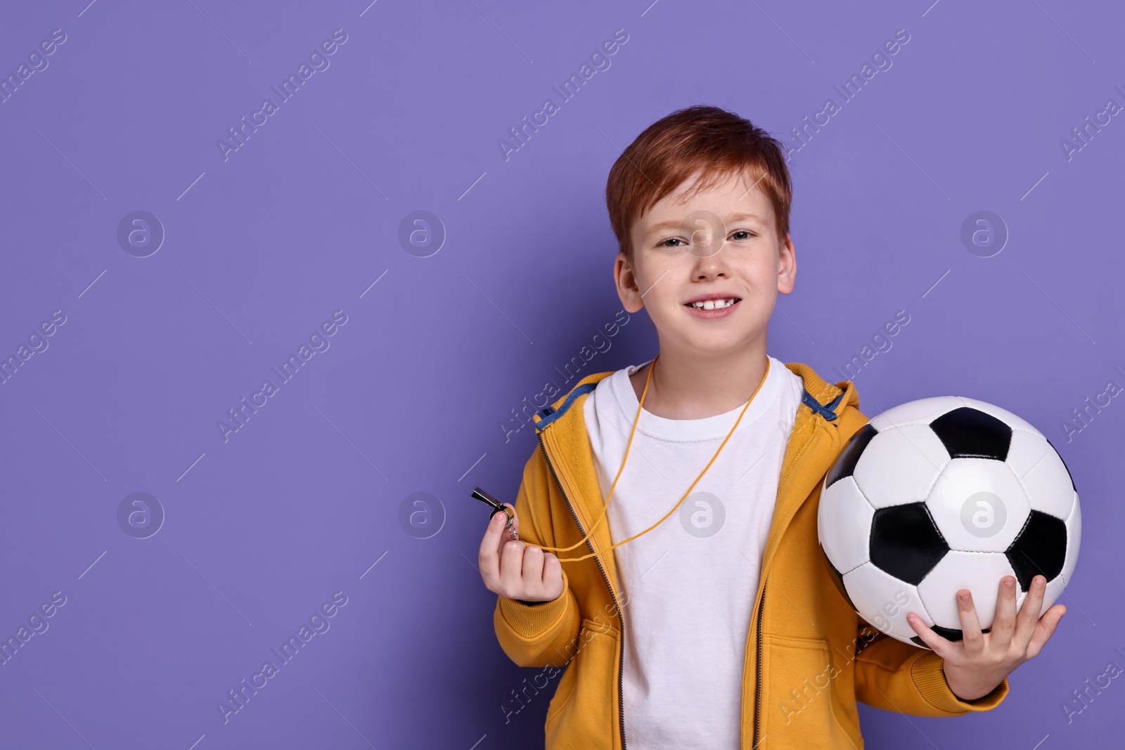 Photo of Little boy with whistle and soccer ball on purple background, space for text