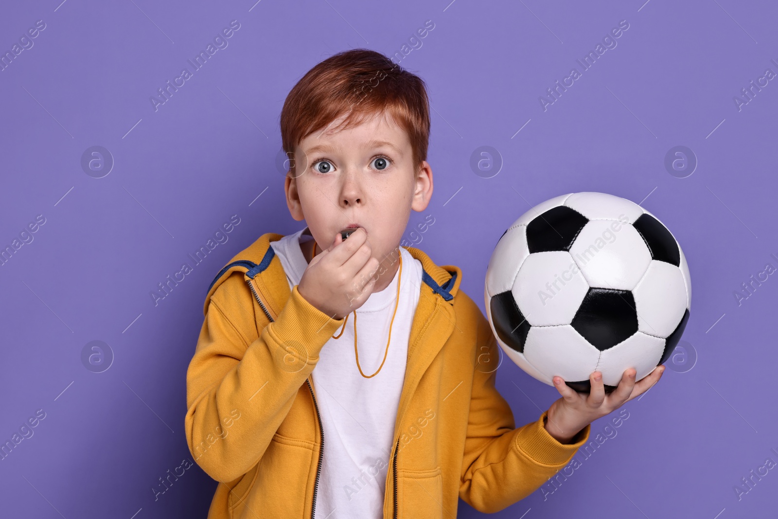 Photo of Little boy with soccer ball blowing whistle on purple background