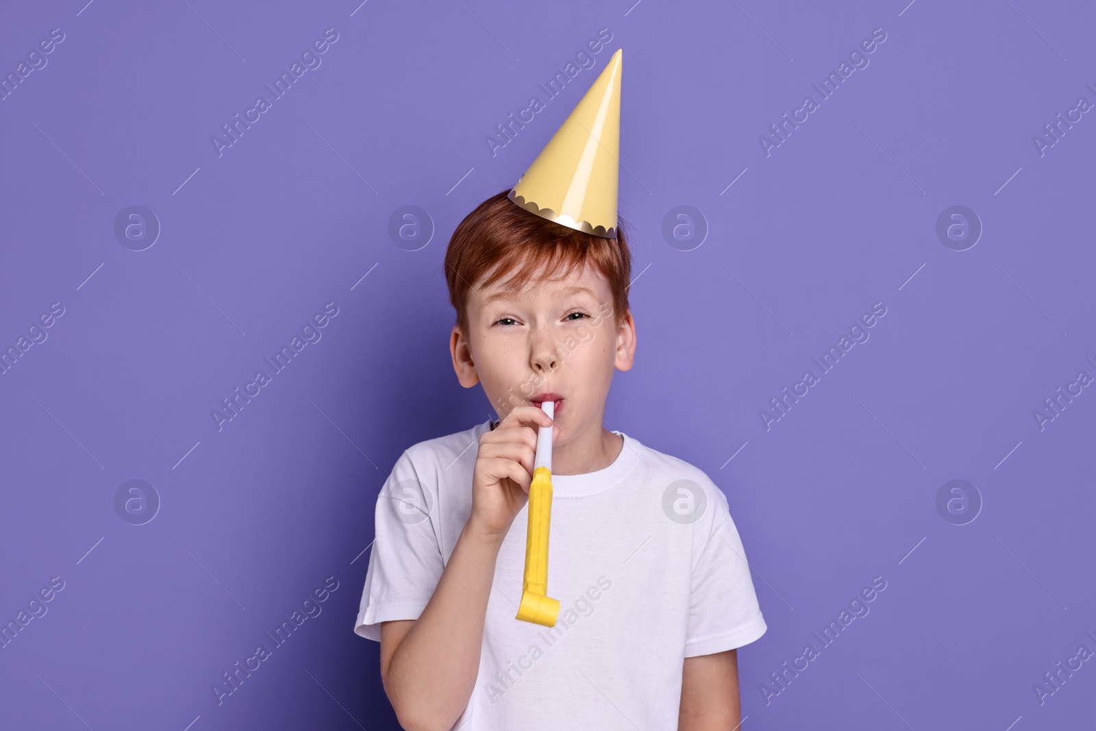 Photo of Little boy in party hat with blower on purple background