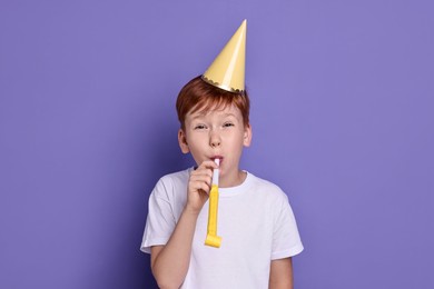 Photo of Little boy in party hat with blower on purple background