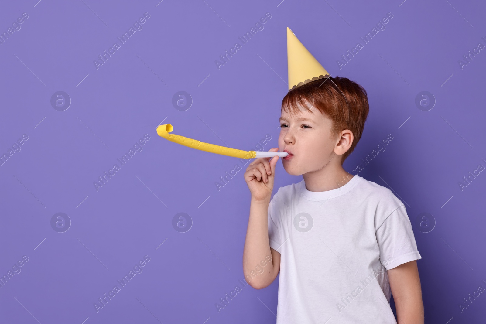 Photo of Little boy in party hat with blower on purple background, space for text