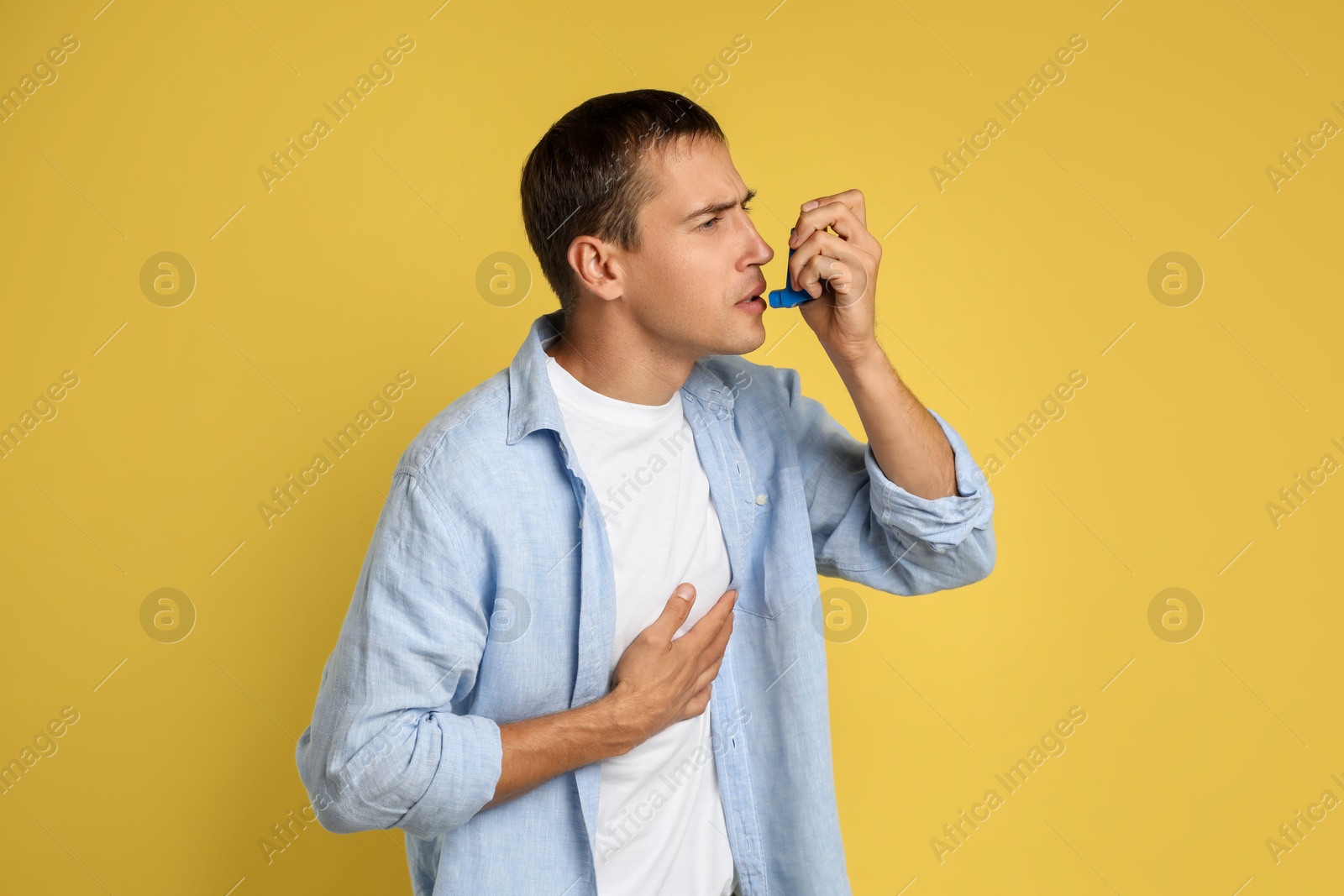 Photo of Man using asthma inhaler on yellow background