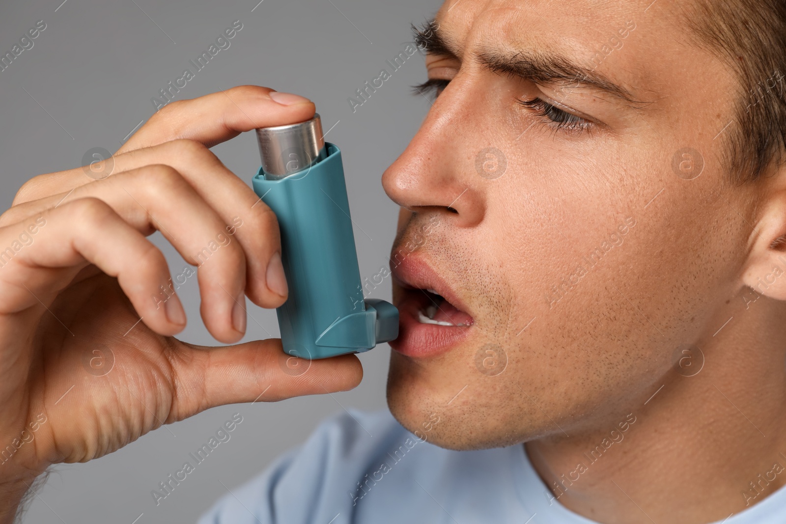 Photo of Man using asthma inhaler on grey background, closeup