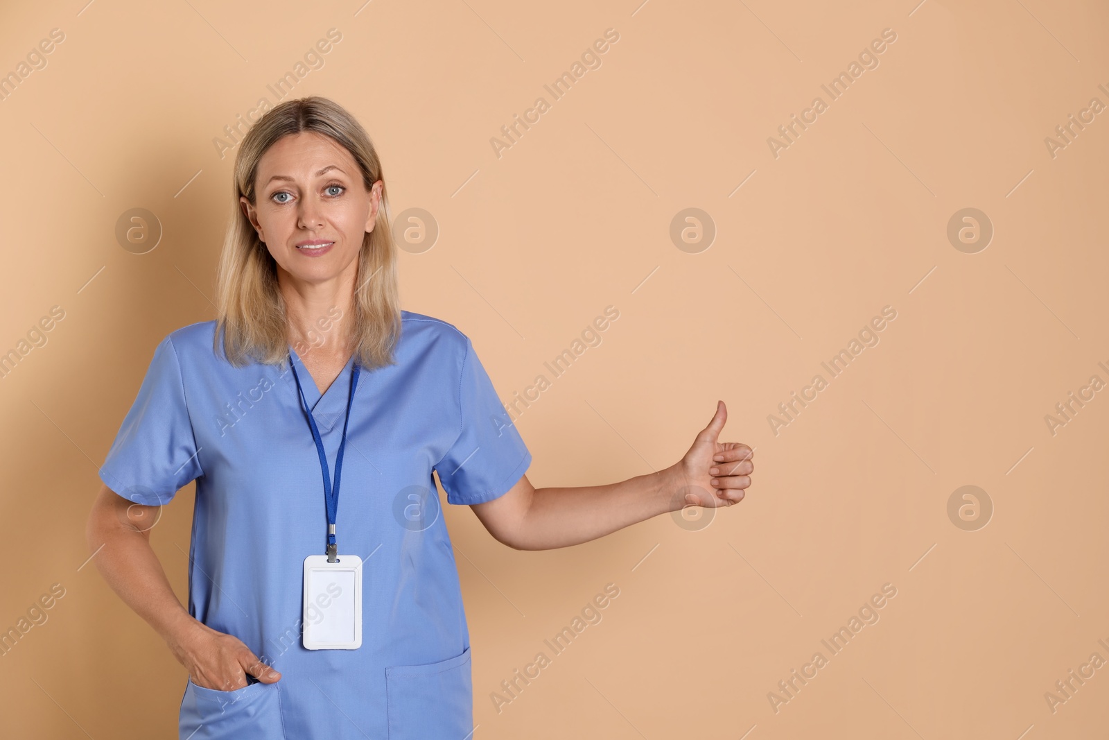 Photo of Nurse in medical uniform with badge showing thumbs up on beige background