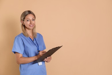 Photo of Nurse in medical uniform with badge and clipboard on beige background, space for text