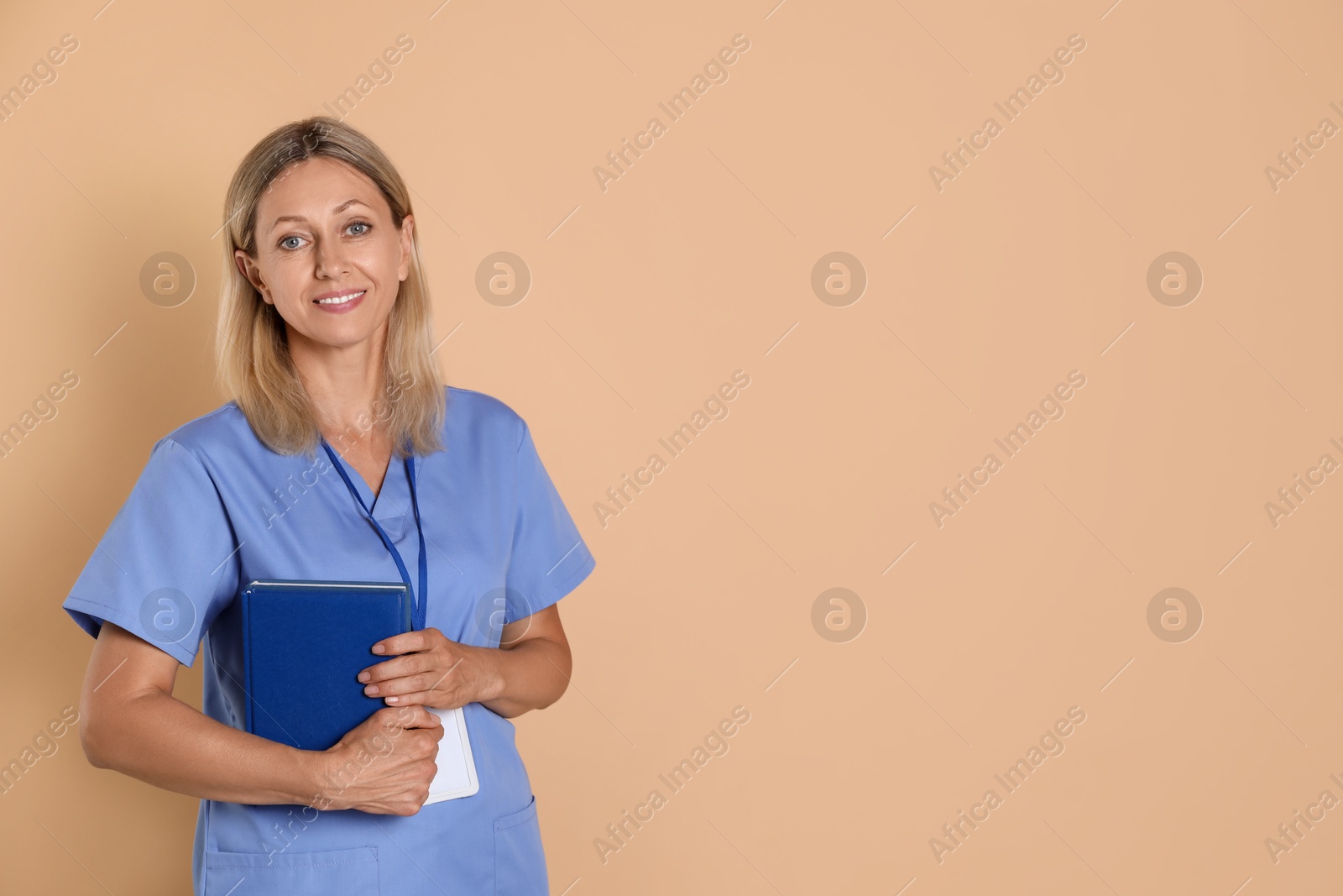 Photo of Nurse in medical uniform with badge and books on beige background, space for text