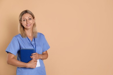 Photo of Nurse in medical uniform with badge and books on beige background, space for text