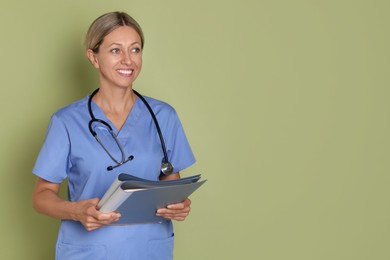 Nurse in medical uniform with folders on light green background, space for text