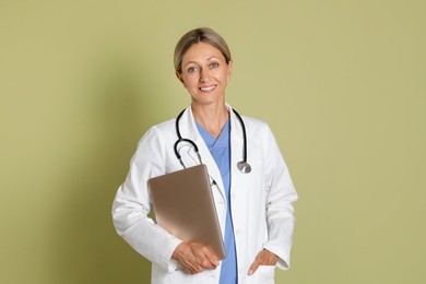 Doctor in medical uniform with stethoscope and laptop on light green background